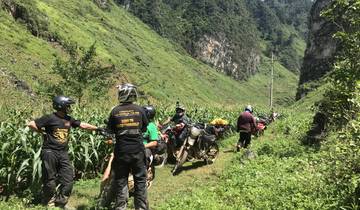 A group of people with motorbikes in a lush, green landscape.