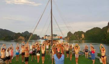 A group of people doing exercises on a boat with scenic limestone cliffs around.