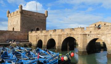 Historic fortified walls with boats floating in a Mediterranean harbor.