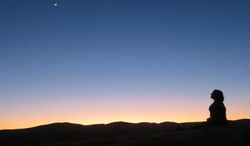 Silhouette of a person meditating against a sunset in a desert.