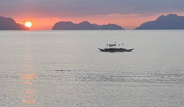 Sunset over a calm sea with a traditional boat.