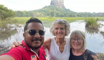 Three people posing in front of a large rock formation and lake