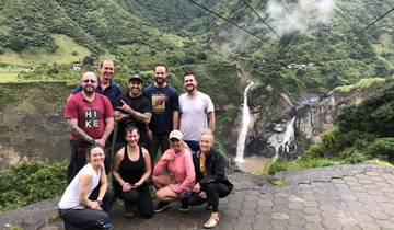 Group of people posing with a distant waterfall in a green valley.