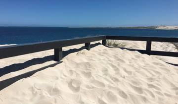 Sandy dunes overlooking the ocean with clear blue sky.