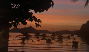 Silhouette of boats on a calm water body with a colorful sunset.