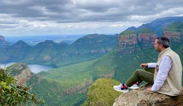 Person sitting on a cliff edge overlooking a mountainous valley.