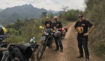 Motorcyclists posing with their bikes on a dirt path surrounded by mountainous terrain.