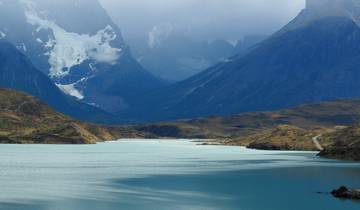 A calm lake with mountains and low clouds in the background.