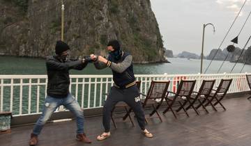 Two people play fighting on a boat deck with limestone cliffs in the background.