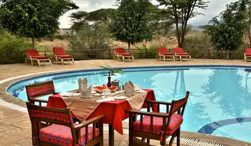 Dining setup by a pool with red chairs, greenery around.