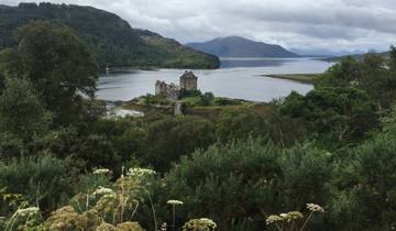 A castle surrounded by lush greenery with a loch view.