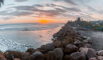 Sunset over a rocky beach with dramatic clouds.