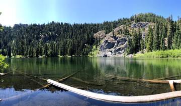 Calm lake surrounded by pine trees and rocky cliffs.