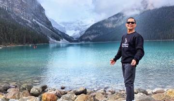 Person posing by a lake with mountain scenery.