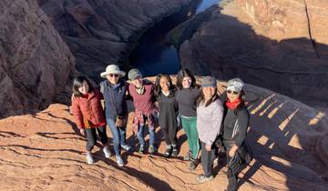 A group of people standing at the edge of a canyon with a river in the background.