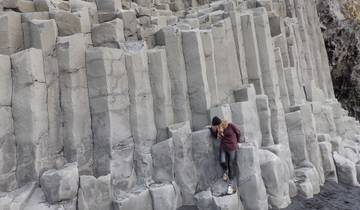 Person climbing basalt columns near the coast.