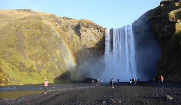 Waterfall with a small rainbow, surrounded by visitors and cliffs.