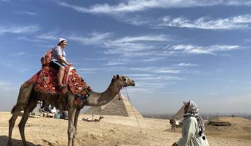Person riding a camel with pyramids in the background.