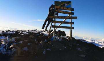 Summit sign for Mount Kilimanjaro with snow and climber.