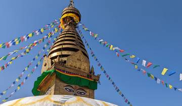 A stupa with prayer flags against a blue sky.