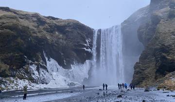 Tall waterfall surrounded by cliffs and people standing below.