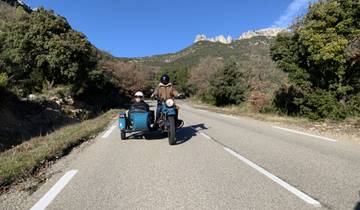 Two people riding a motorcycle with a sidecar on a country road.