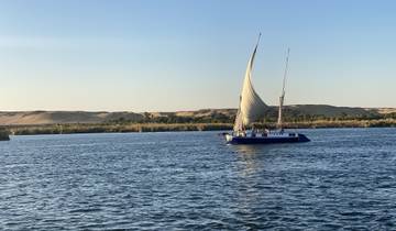 A sailboat on the Nile River with sandy dunes in the background.
