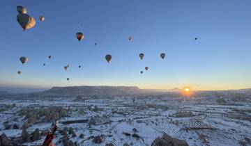 Hot air balloons floating over a snowy landscape at sunrise.