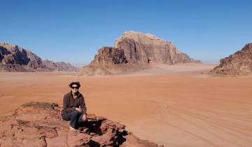 Person sitting on a rocky outcrop with a vast desert landscape in the background.