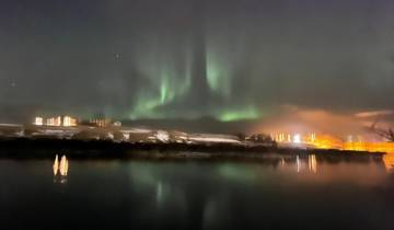 Northern Lights over a snowy landscape with water reflecting the lights.