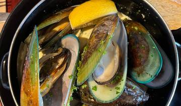 A dish of steamed mussels with a lemon wedge and broth.