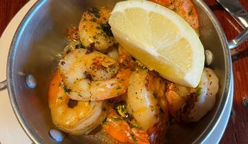 A dish of grilled prawns with a lemon wedge in a metal bowl.