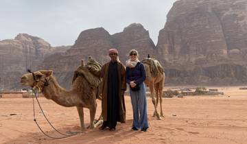 Two people with camels in the desert with rocky hills.