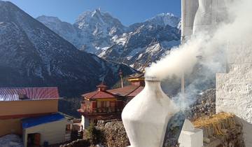 Smoke rising from a religious site against a backdrop of snow-covered mountains.