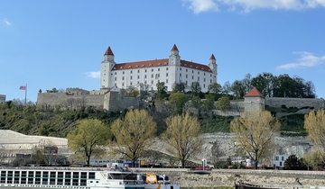 A large castle on a hill overlooking the river with trees around.