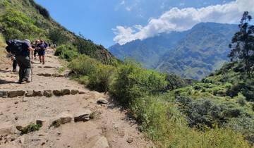 People hiking on a mountainous trail with lush greenery.