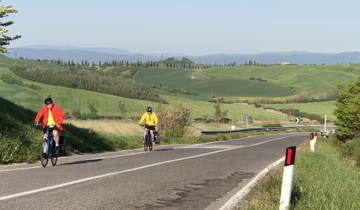Two cyclists riding on a rural road with scenic green hills.