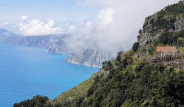 A panoramic mountain and coastal view with a house perched on the edge.
