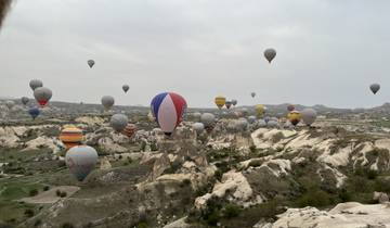 Many hot air balloons in the sky over Cappadocia's rock formations.
