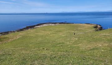 Coastal landscape with rolling grasslands and a distant view of a calm sea.