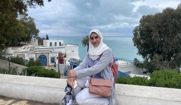 A person sitting on a ledge with a scenic view of the sea and buildings below.