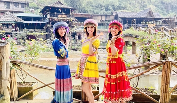 Three women in colorful traditional attire posing in a cultural village.