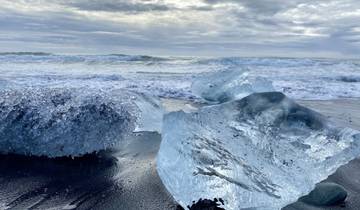Clear ice on black sand beach with ocean waves.