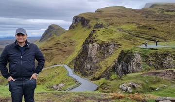 Hiker standing on a winding road with cliffs in the background.