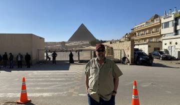 Man standing in front of the pyramid in a desert area.
