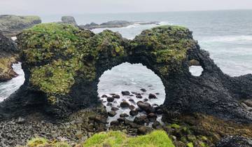 Coastal rock formation with natural arches and the ocean.