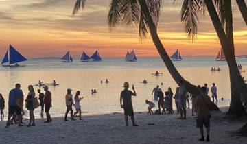 People enjoying a sunset at the beach with sailboats.