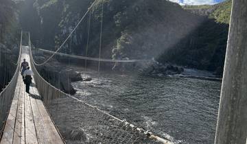 People crossing a rope bridge over a river in the mountains.