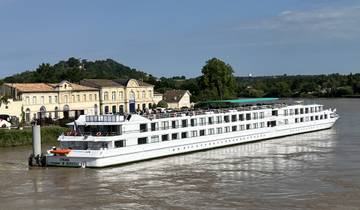 Large cruise ship docked by riverside buildings.