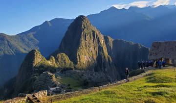 Machu Picchu with visitors and lush surroundings under a clear sky.